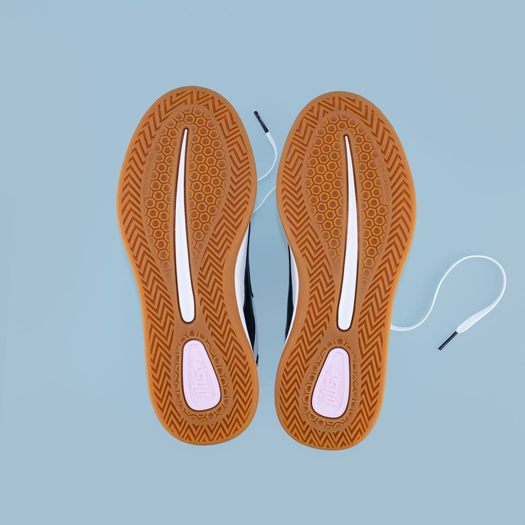 Bottom view of PB5STAR Cosmic sneakers showing gum rubber outsoles with tread pattern and traction pods, displayed on light blue background.