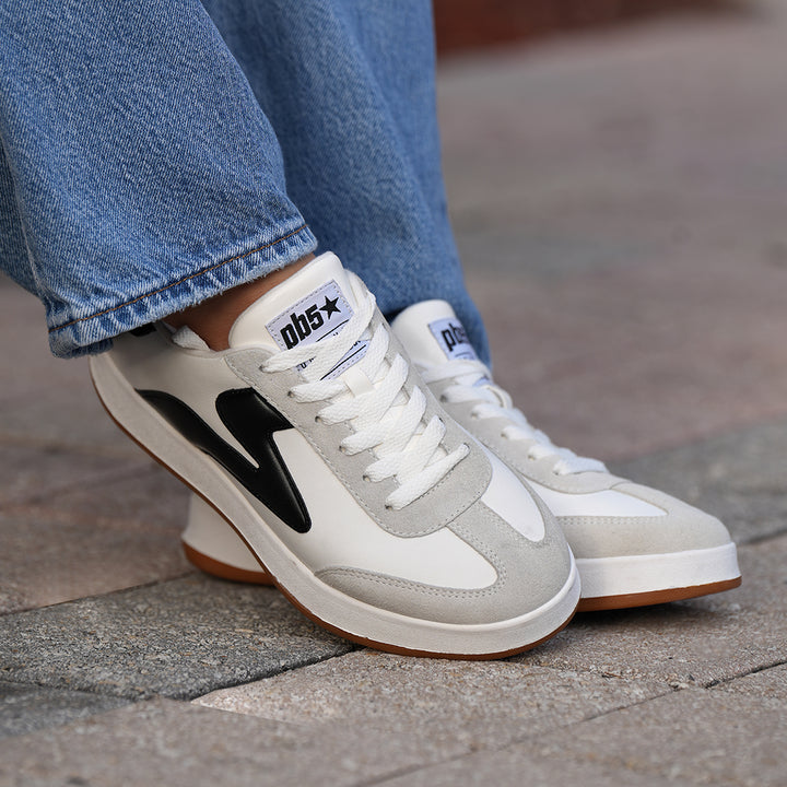 Close-up of PB5star Cosmic sneakers in white and black worn with jeans, showing lace detail, side logo, and gum rubber sole