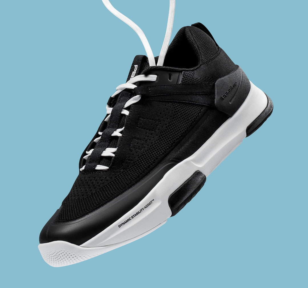 Men's black and white PB5 Court2 pickleball shoe floating on blue background