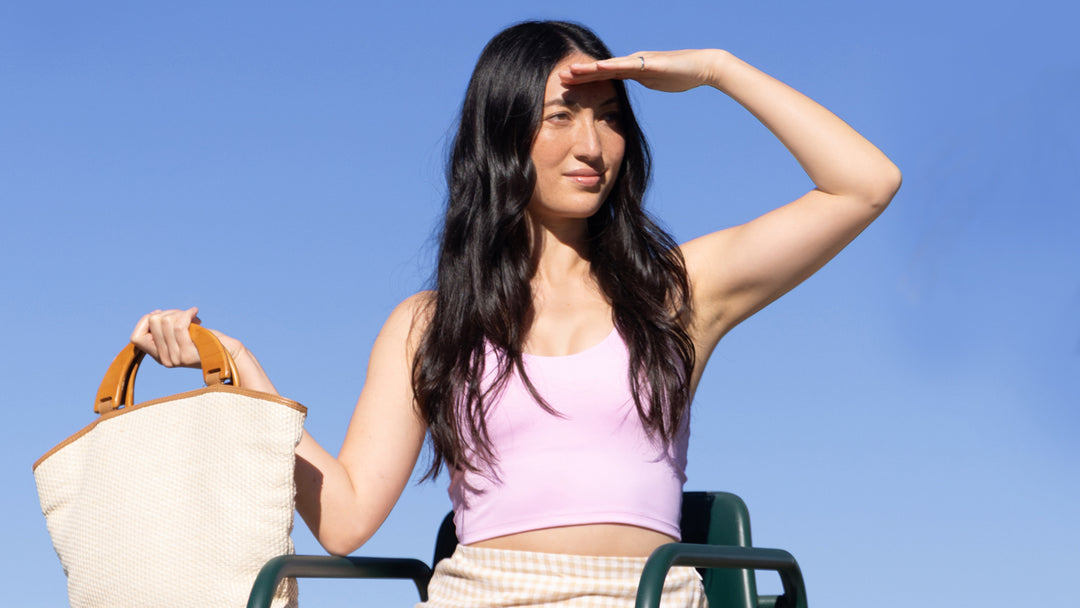 Lifestyle image of a woman in a pink top looking into the distance against a blue sky
