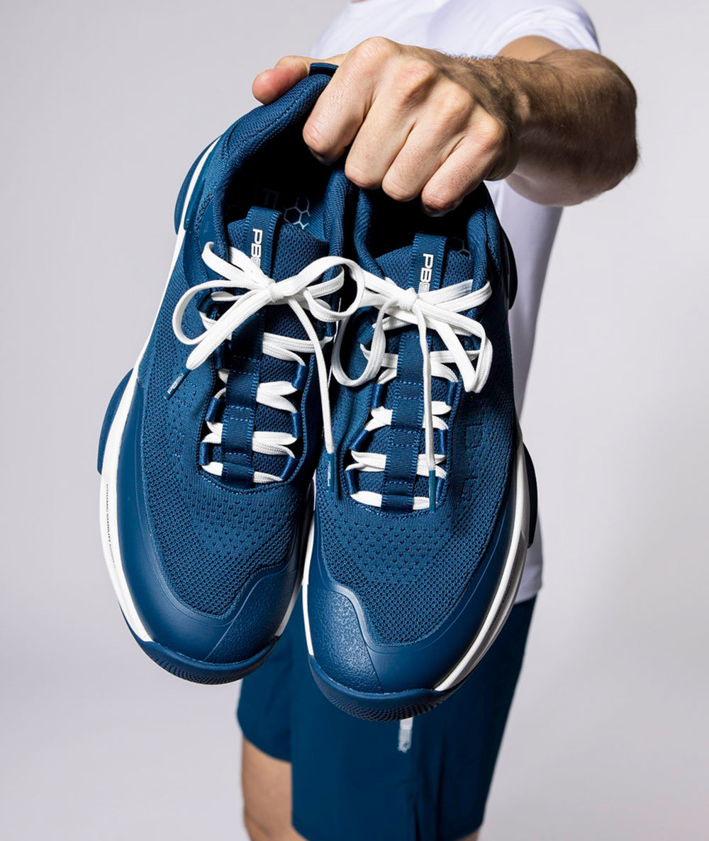 A pair of PB5star Court2 in Men's Astral Blue held up to camera by male hand for close up shot