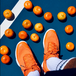 Pickleball court with Tangerine PB5 Court2s on feet next two a bunch of tangerines.