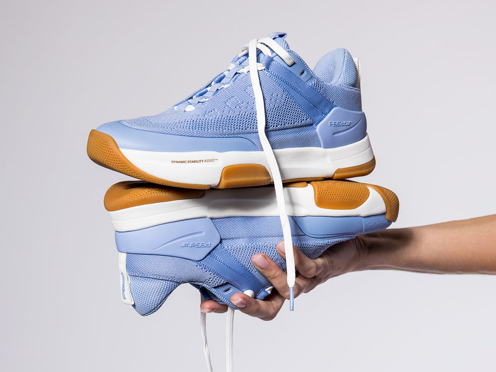 Pair of women’s Court2 pickleball shoes in lilac with gum soles, held in hand against light background