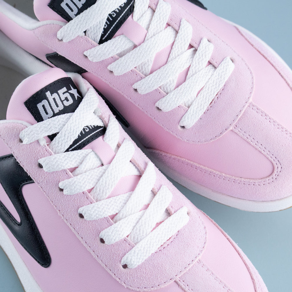 Pink sneakers with white laces and black accents on a light gray background
