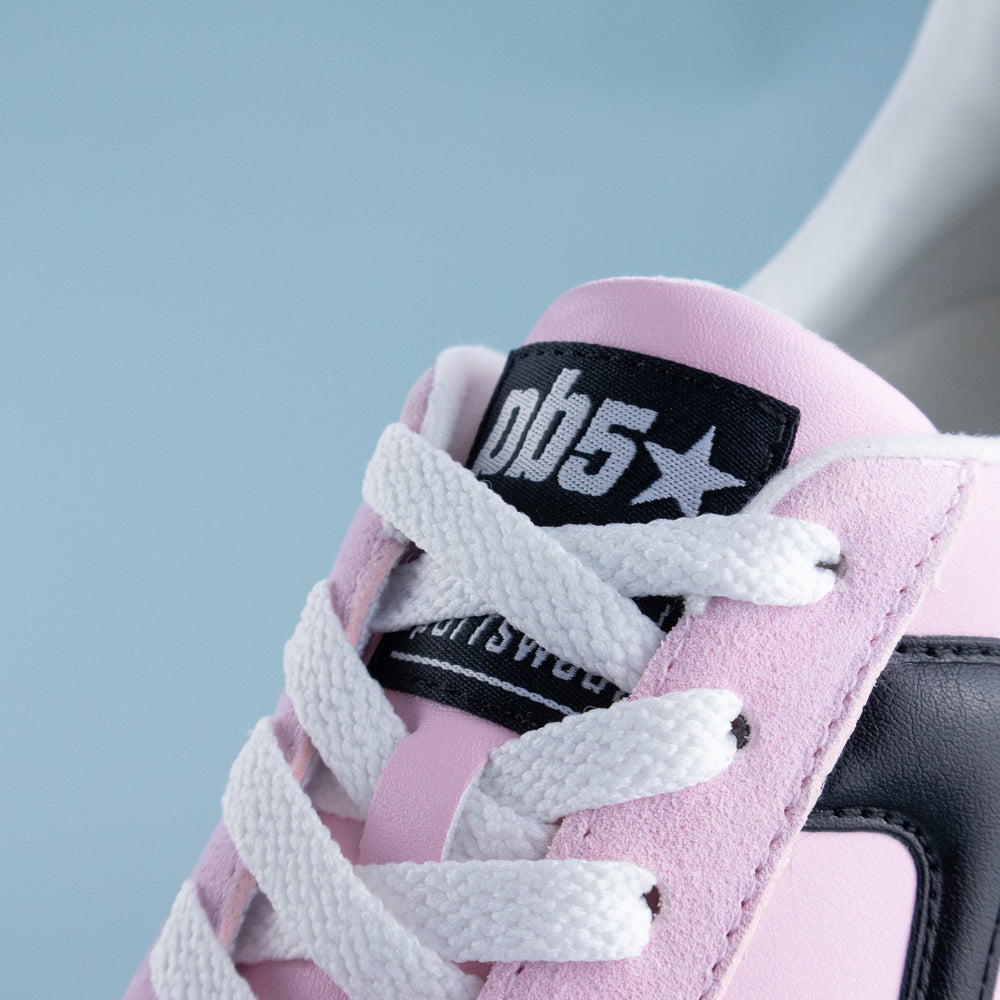 Pink sneaker with white laces and a black label on a light blue background